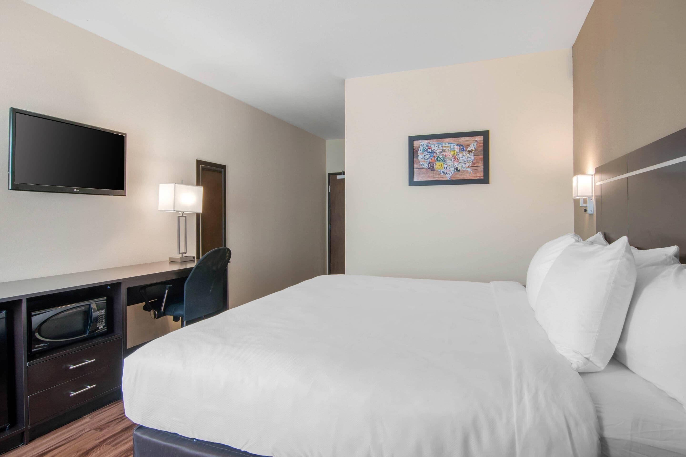 Ein Hotelzimmer mit Bett, Schreibtisch, Flachbildfernseher, Mikrowelle und Stuhl.