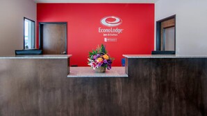 A reception area with a red wall, a logo for Econo Lodge Inn & Suites, and a flower arrangement on the counter. - Econo Lodge Inn & Suites Springfield Main Street (Springfield)