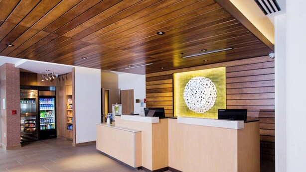 A reception area with a wooden ceiling, a reception desk, a wall-mounted decorative item, and a vending machine. - Fairfield Inn & Suites Philadelphia Broomall/Newtown Square (Broomall)