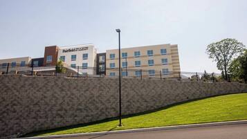 A hotel named Fairfield by Marriott with a stone wall and a grassy area in front.