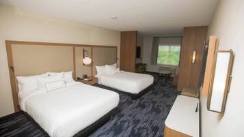 A hotel room with two beds, a desk, a chair, a small table, and a window with a view.