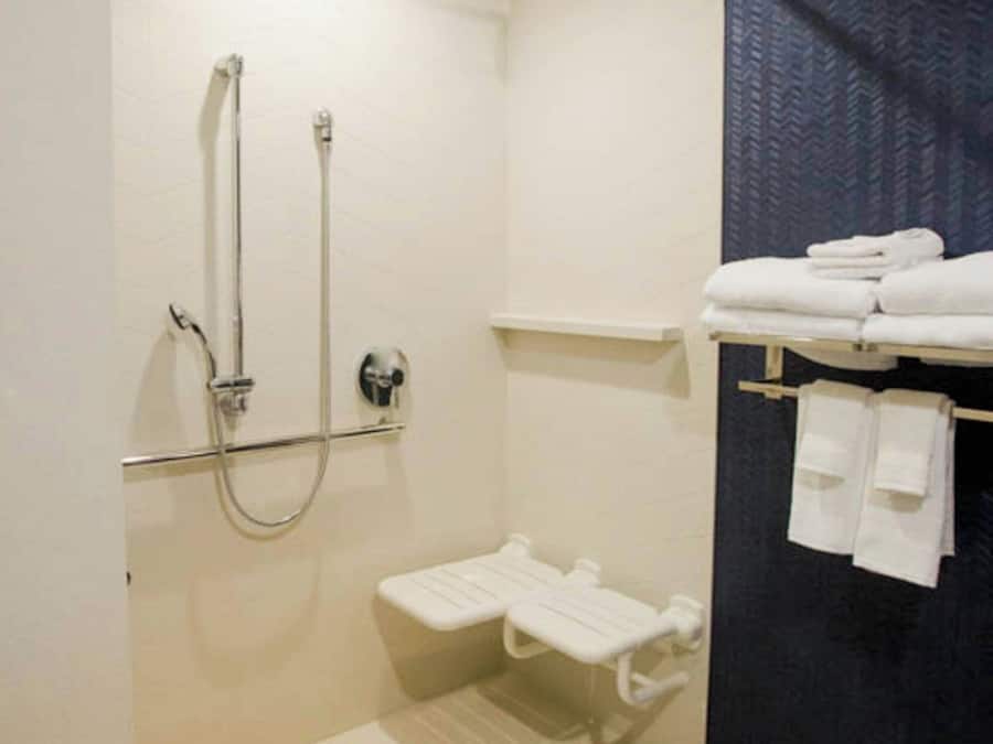Un baño moderno con ducha a nivel, inodoro y un perchero con toallas dobladas.