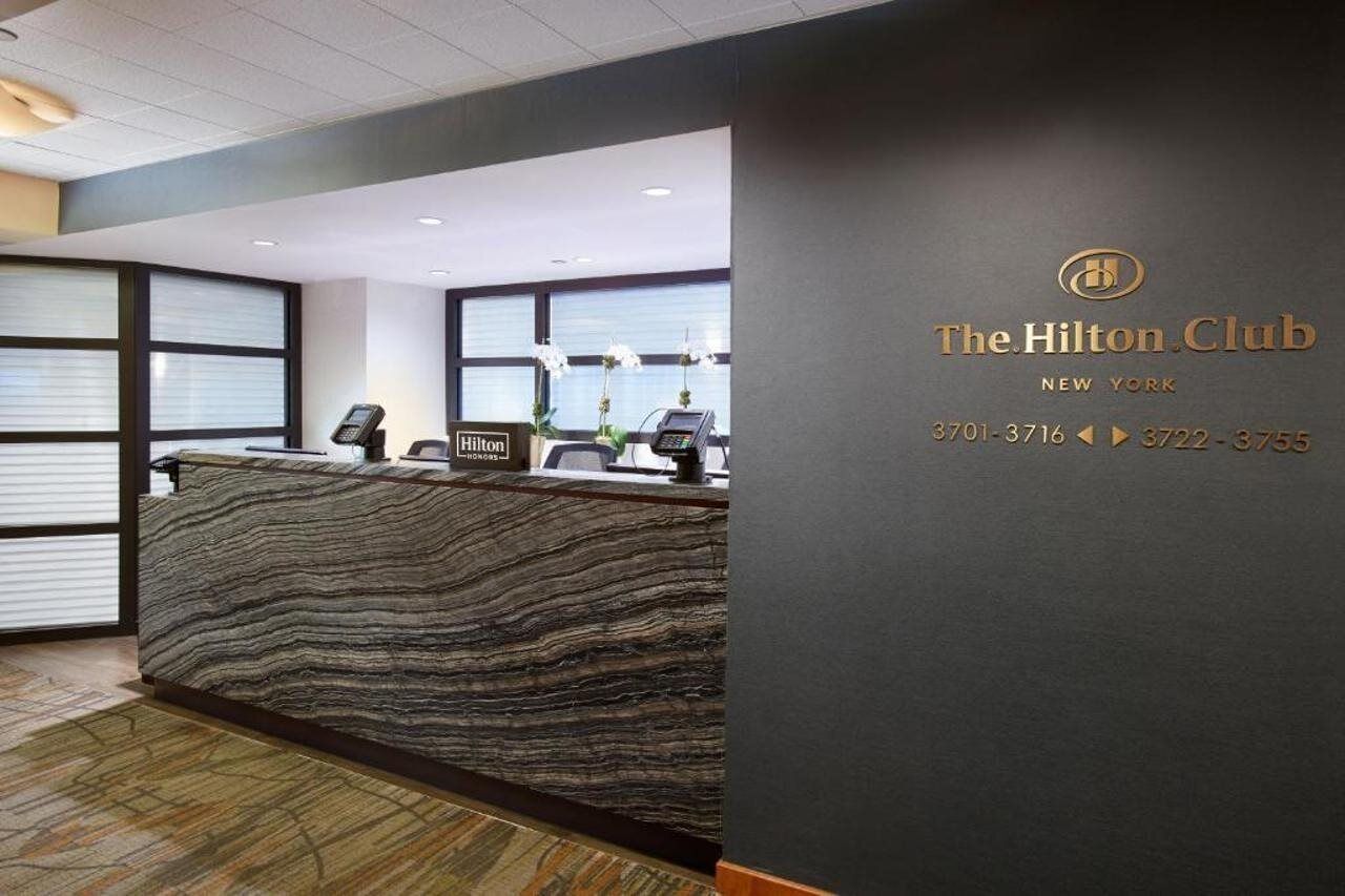 A reception desk at The Hilton Club in New York with a modern design, a phone, and a sign.