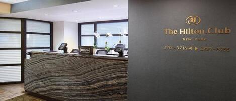 A reception desk at The Hilton Club in New York with a modern design, a phone, and a sign.