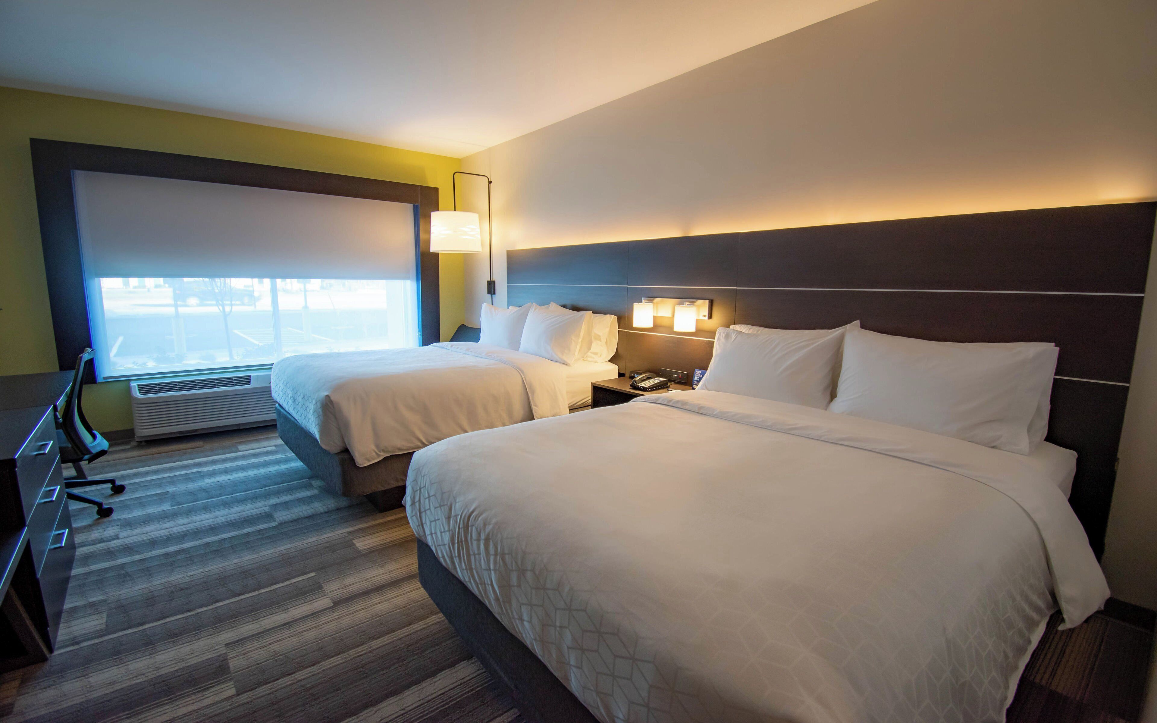 Habitación de hotel con dos camas, un escritorio, una silla, una lámpara y un ventanal grande.
