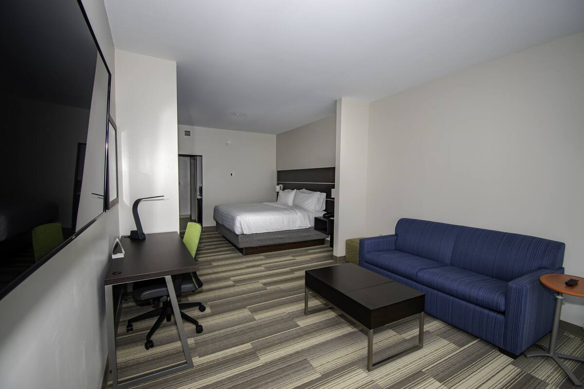 Una camera d'albergo con un letto, un divano blu, una scrivania con una sedia e un tavolino.