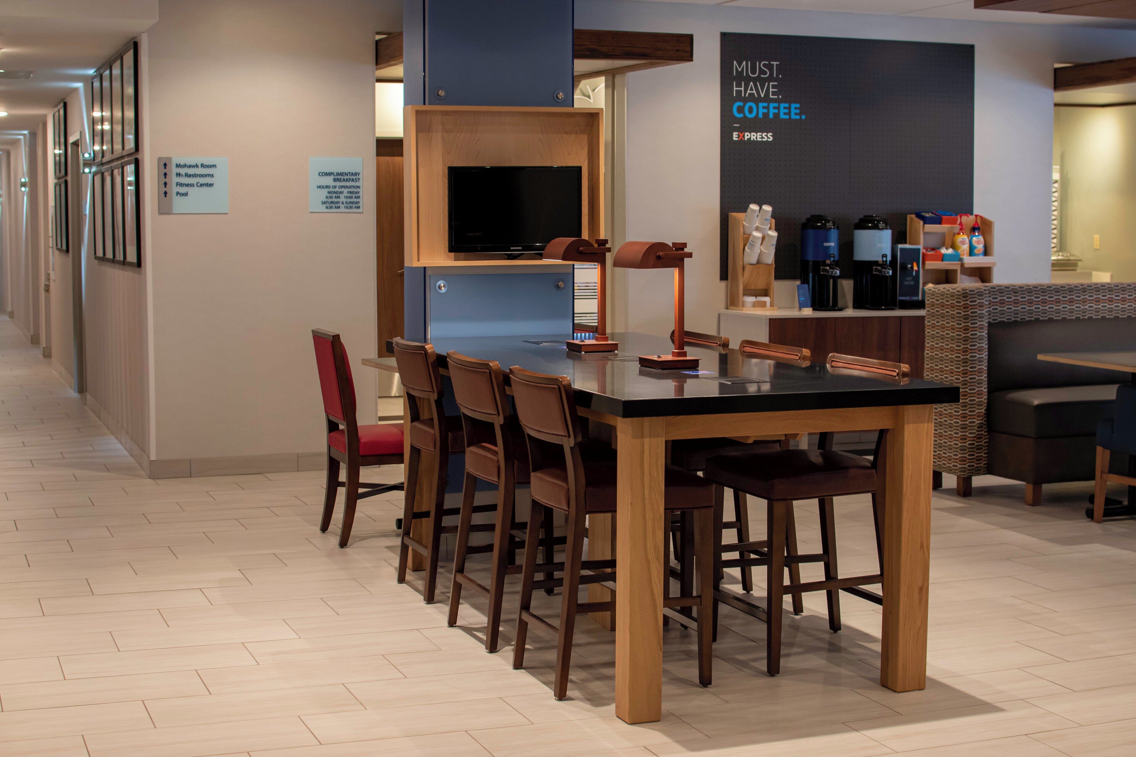 A hotel lobby with a reception desk, a coffee station, and a seating area with a table and chairs.