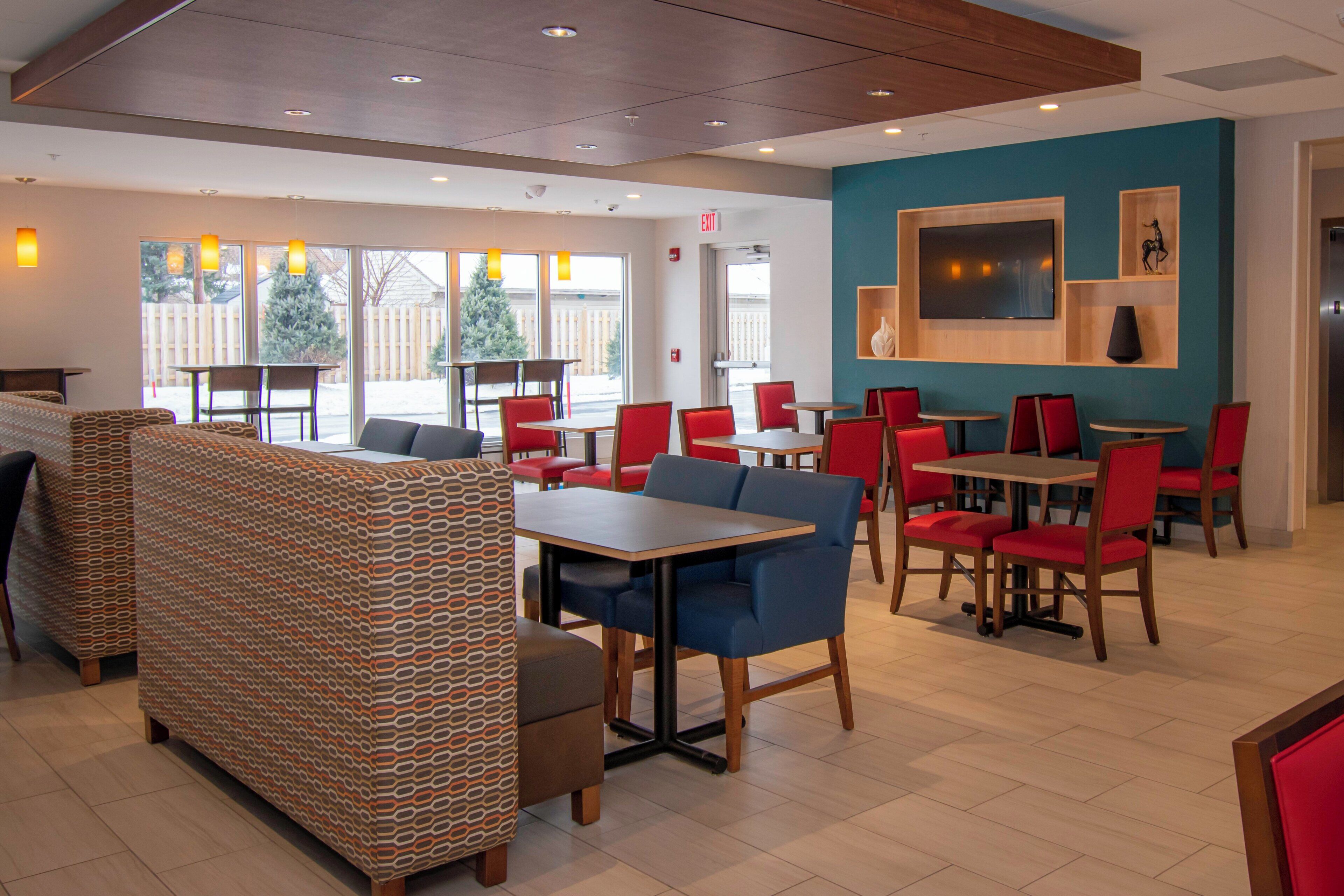 A restaurant with booths, tables, and chairs. There is a TV mounted on the wall and a Christmas tree outside.