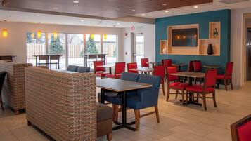 A restaurant with booths, tables, and chairs. There is a TV mounted on the wall and a Christmas tree outside.