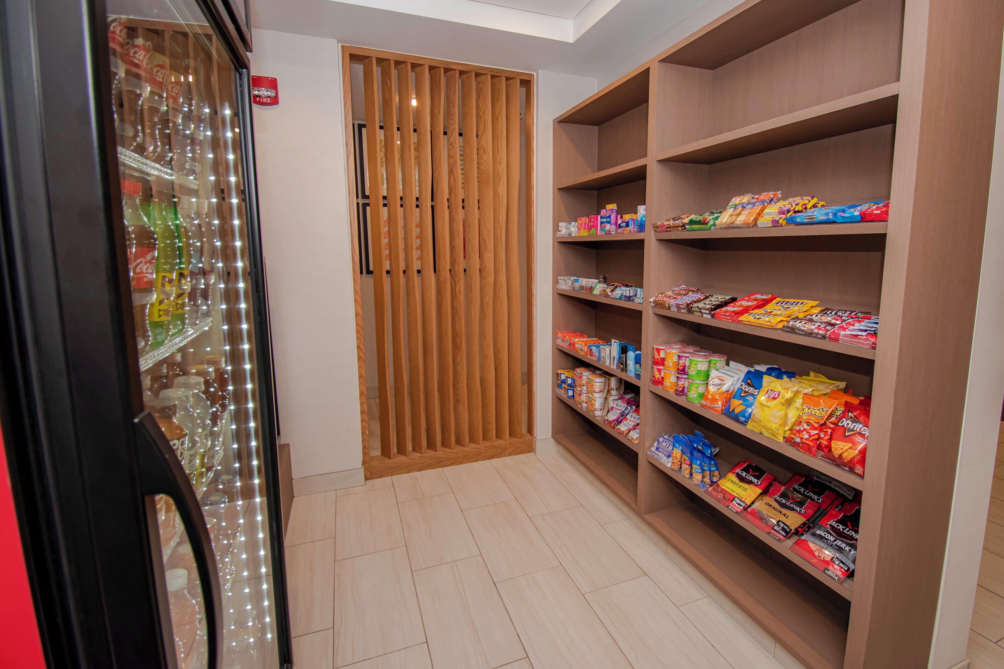 A snack aisle with various packaged goods, a fire alarm, and a refrigerated display with bottles.