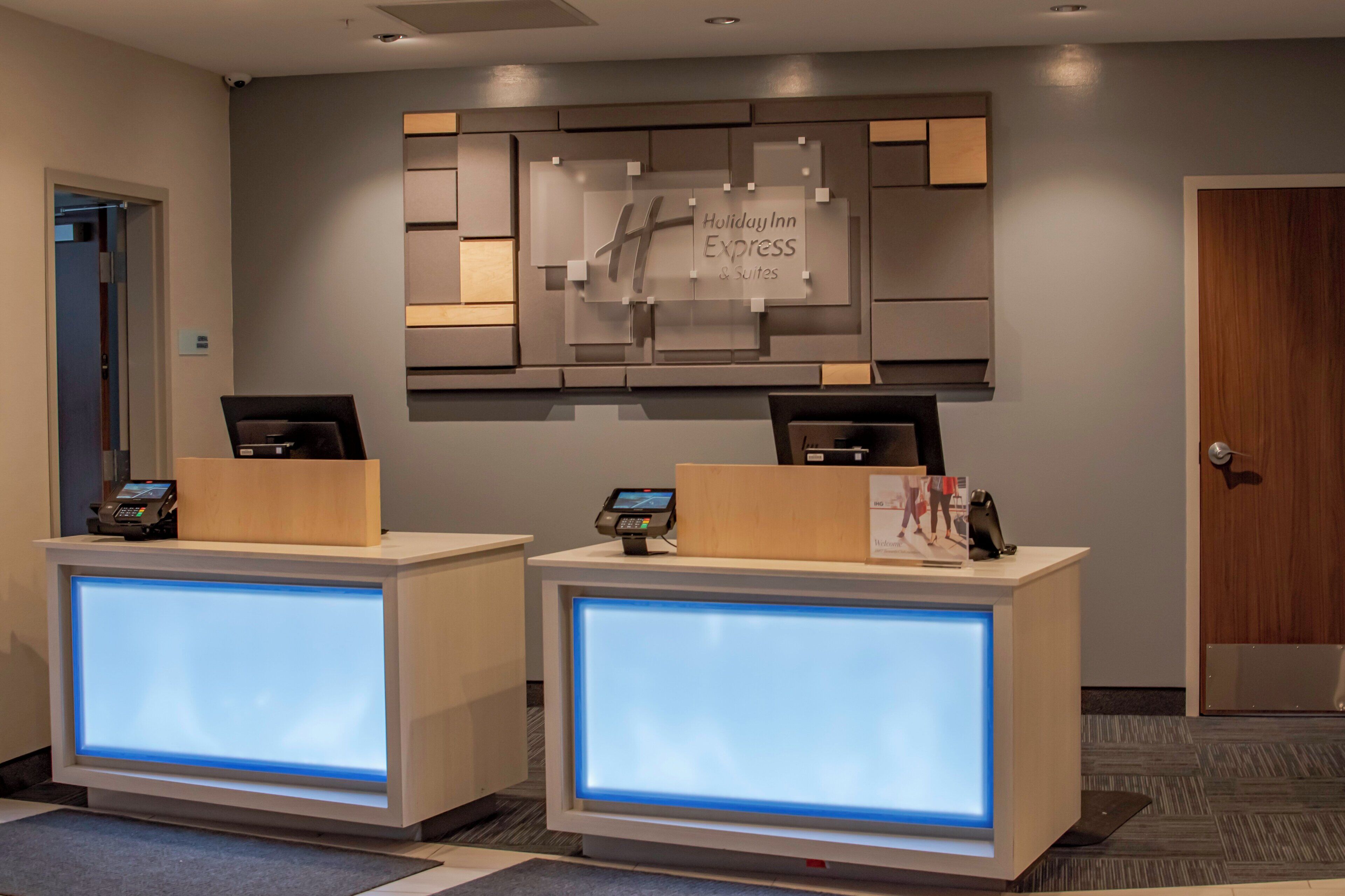 A reception desk with a digital display, a sign for Holiday Inn Express & Suites, and a security camera on the wall.