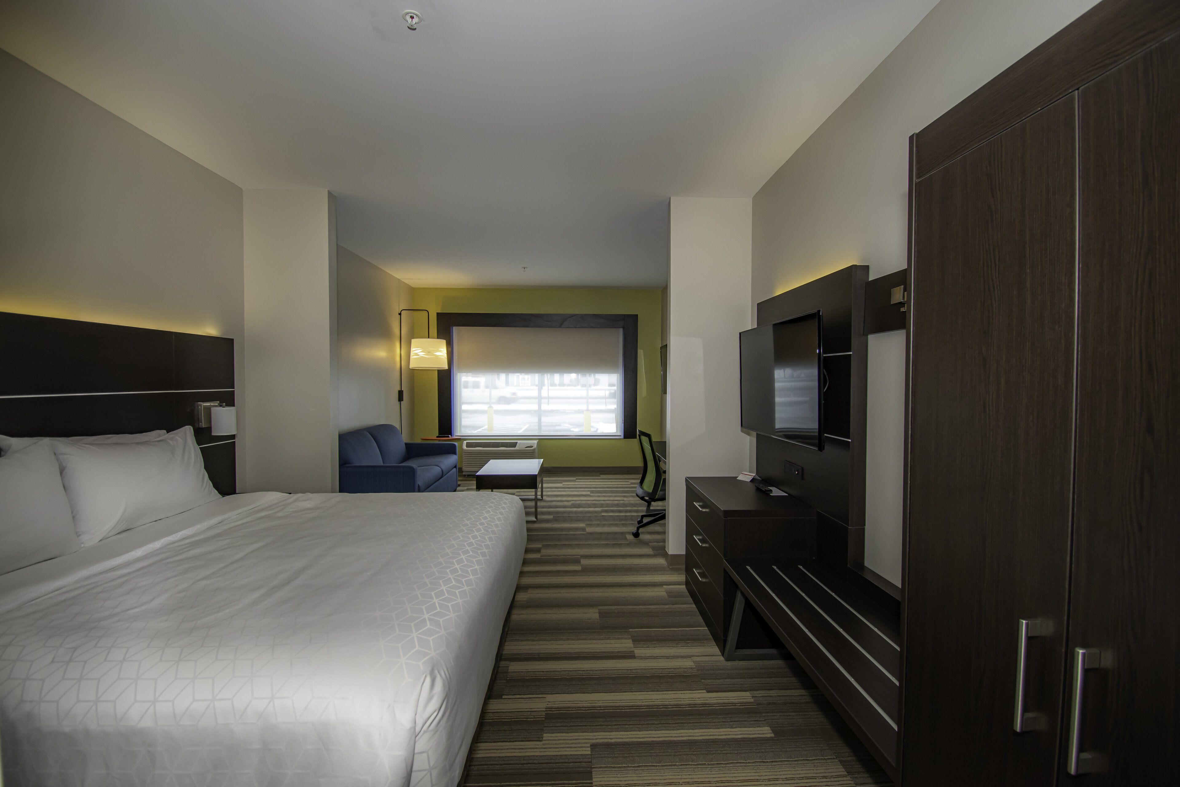 A hotel room with a large bed, a desk, a chair, a television, and a wardrobe.