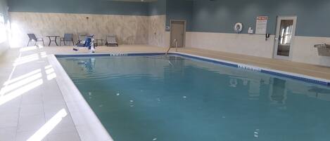 An indoor swimming pool with clear water, surrounded by lounge chairs and a tiled floor.