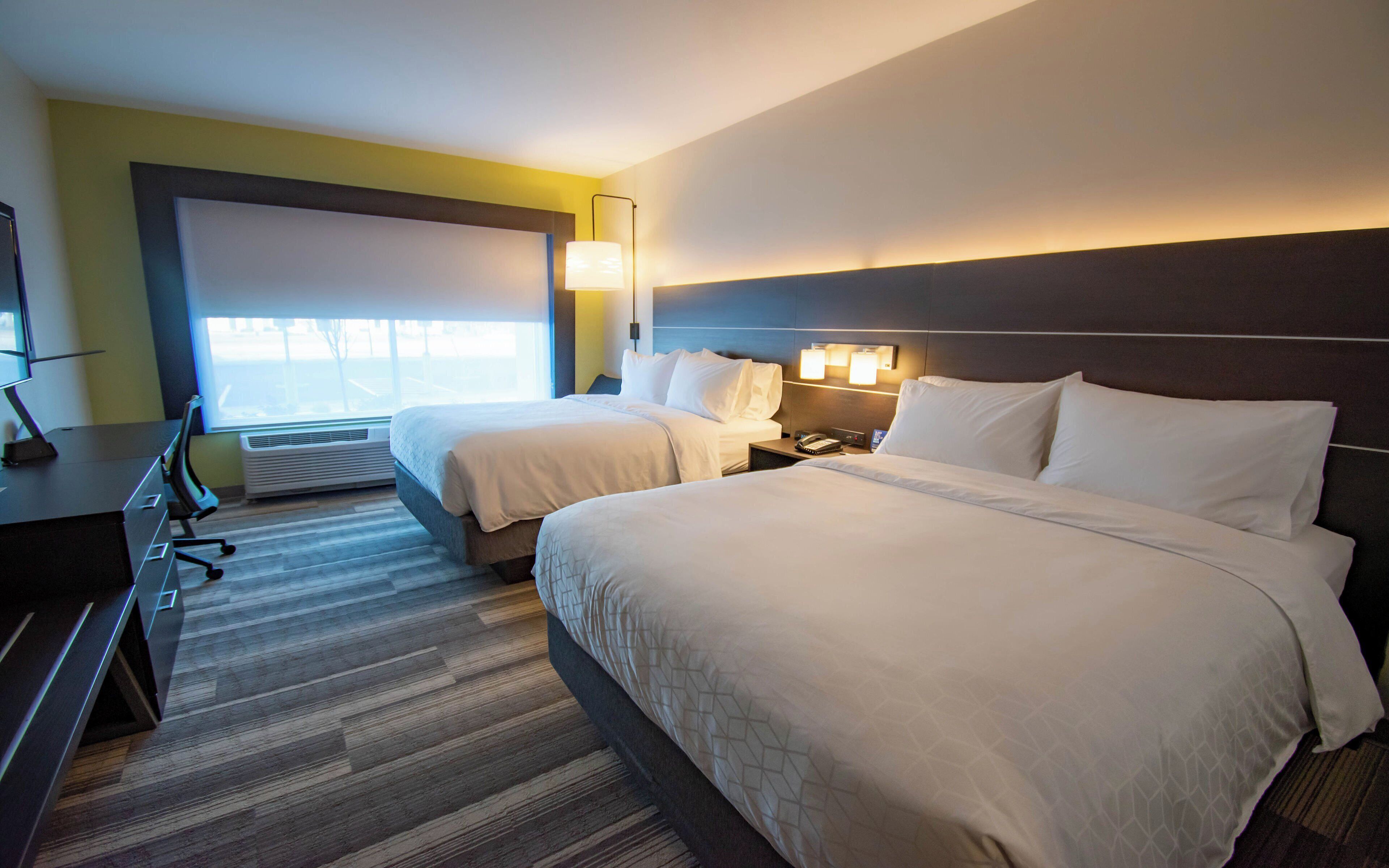 A hotel room with two beds, a desk, a chair, a lamp, and a window.