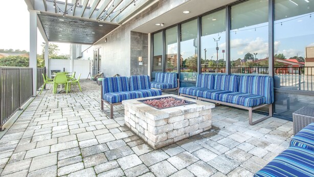 Een terras buiten met stenen vloer, een vuurkorf en blauw gestreepte zitplaatsen.