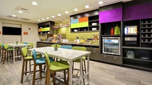 Een modern restaurant met een kleurrijk interieur, inclusief een bord met de tekst 'Inspired table', verschillende zitmogelijkheden en een automaat voor drankjes.