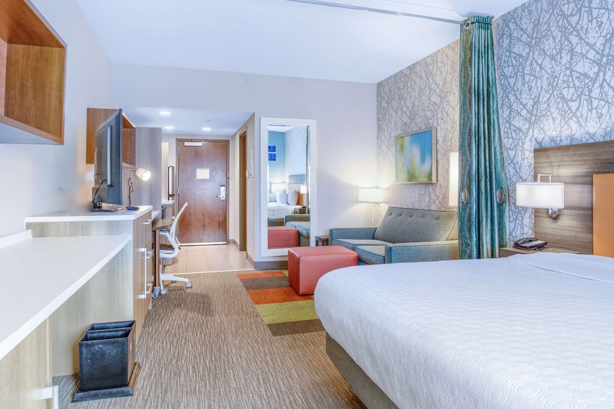 Ein Hotelzimmer mit einem Bett, einem Schreibtisch, einem Sessel, einem kleinen Tisch, einer Lampe und einem Telefon.