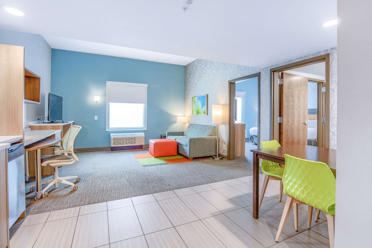 Ein modernes Hotelzimmer mit einer Küchenzeile, einem Sofa, einem Esstisch und einem großen Spiegel.