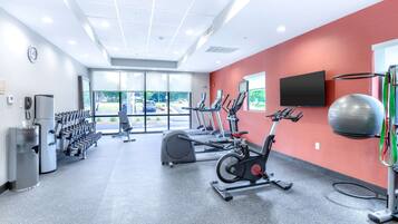 A gym with cardio machines, dumbbells, and a large exercise ball.