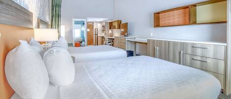 A hotel room with a large bed, a desk, and a kitchenette.