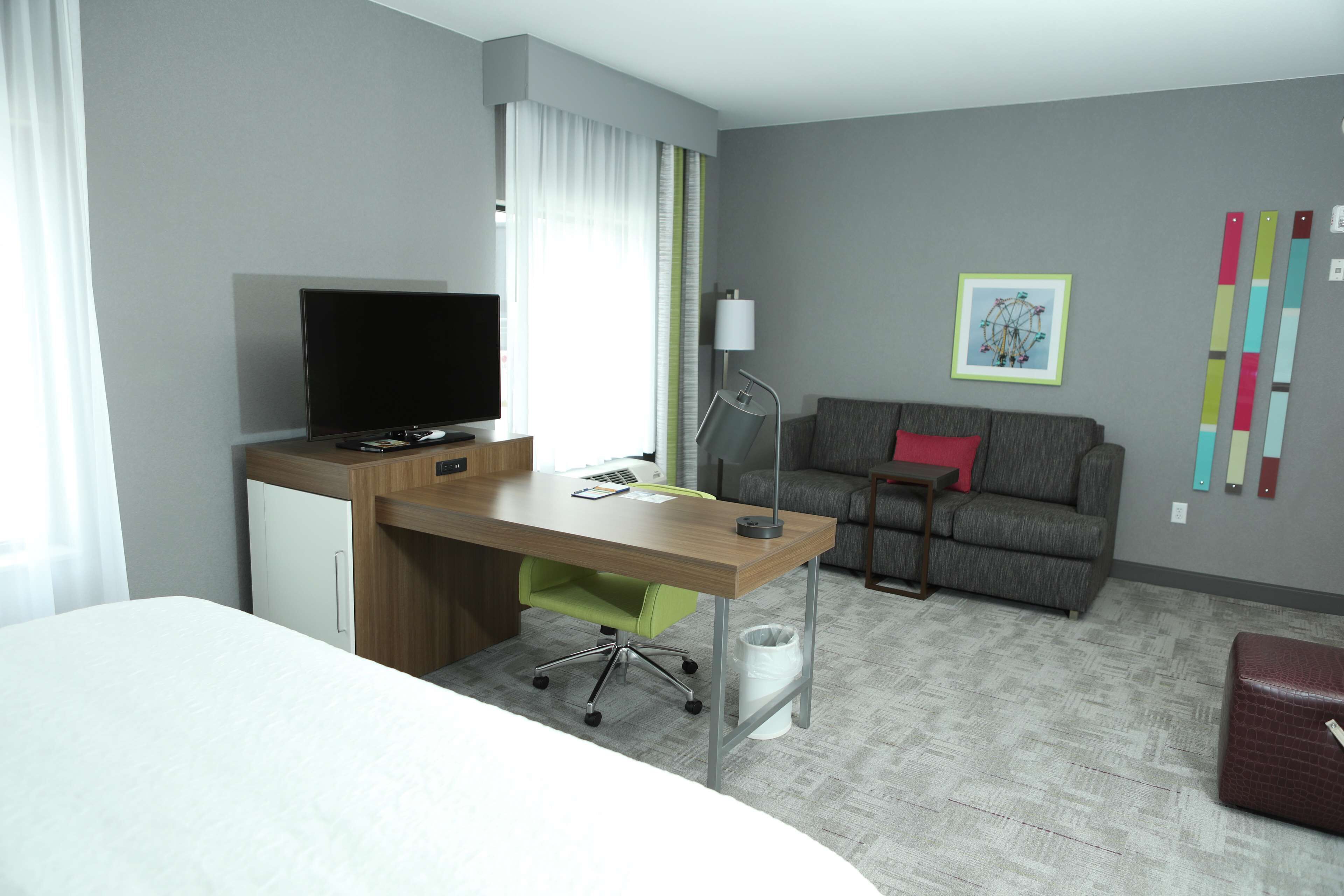 A hotel room with a bed, a desk with a computer, a television, a sofa, and a trash bin.