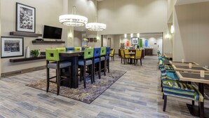 A spacious dining area with multiple tables and chairs, a television on a shelf, and a large chandelier. - Hampton Inn & Suites Burlington (Burlington)