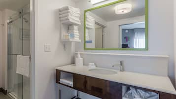 A modern bathroom with a glass shower, white towel stacks, a large mirror, and a sink with a dark vanity.