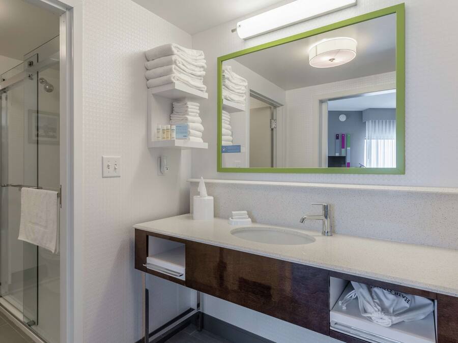 A modern bathroom with a glass shower, white towel stacks, a large mirror, and a sink with a dark vanity.