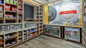 A snack and sundries section with shelves stocked with various products, a chalkboard with 'Snack!' written on it, and a 'Treats' sign above a display case. - Hampton Inn & Suites Burlington (Burlington)