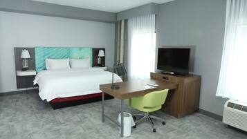 A hotel room with a bed, desk, chair, TV, and a waste bin.