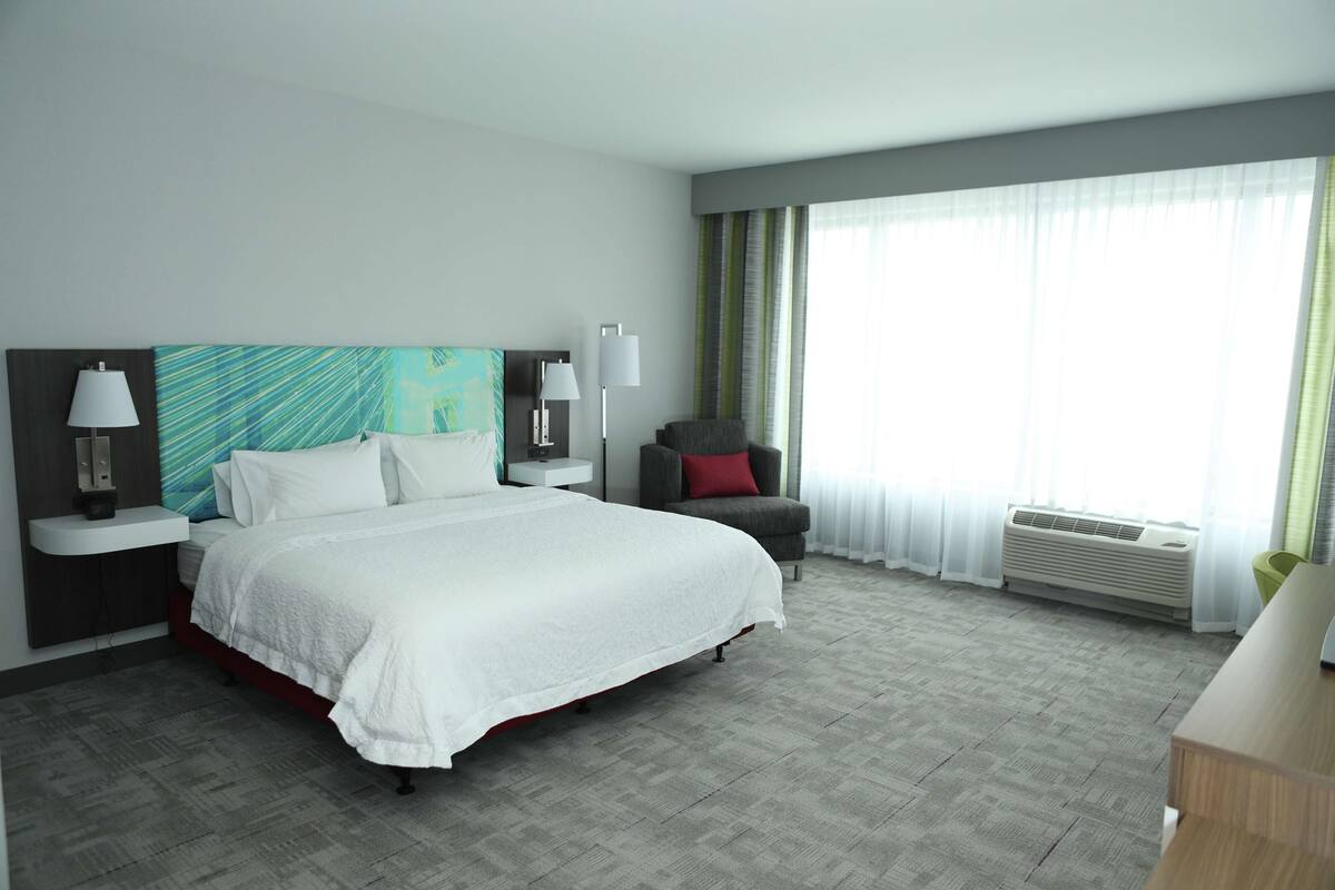 Une chambre d’hôtel avec un grand lit, une chaise, un bureau et une fenêtre avec des rideaux.