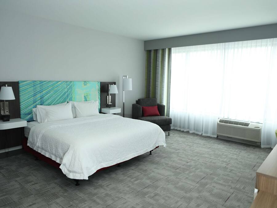 A hotel room with a large bed, a chair, a desk, and a window with curtains.