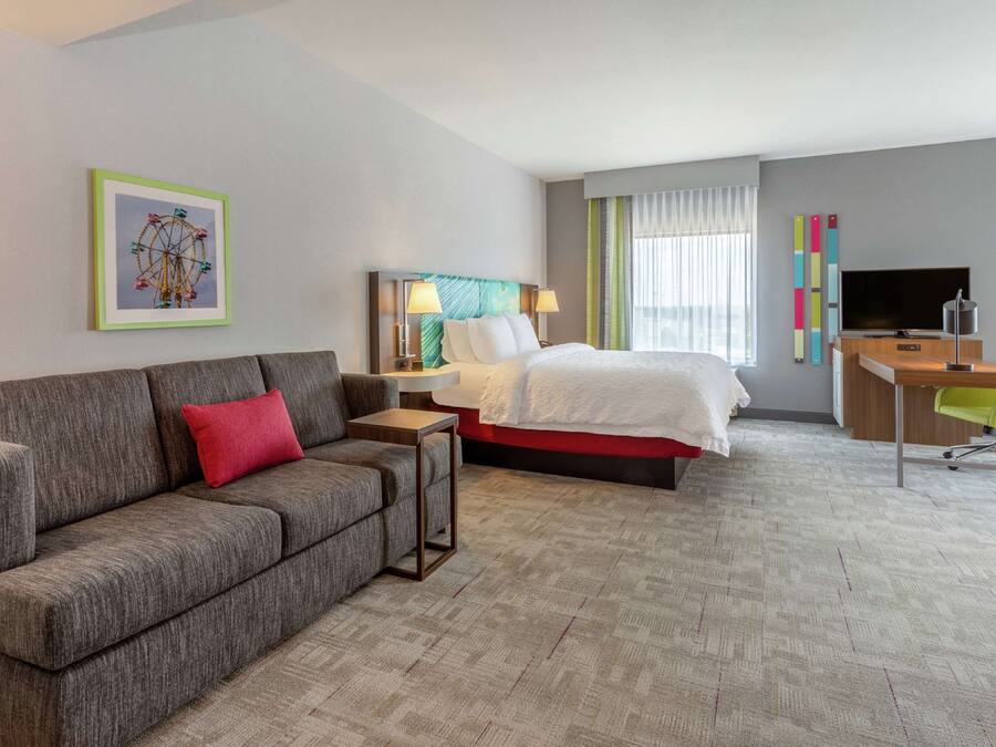 A hotel room with a bed, a sofa, a desk, a TV, and a framed picture on the wall.