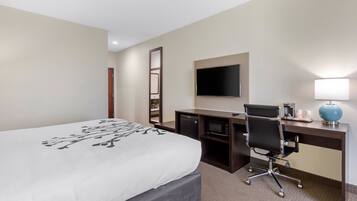 A hotel room with a bed, a desk with a computer, a chair, a TV, and a lamp.
