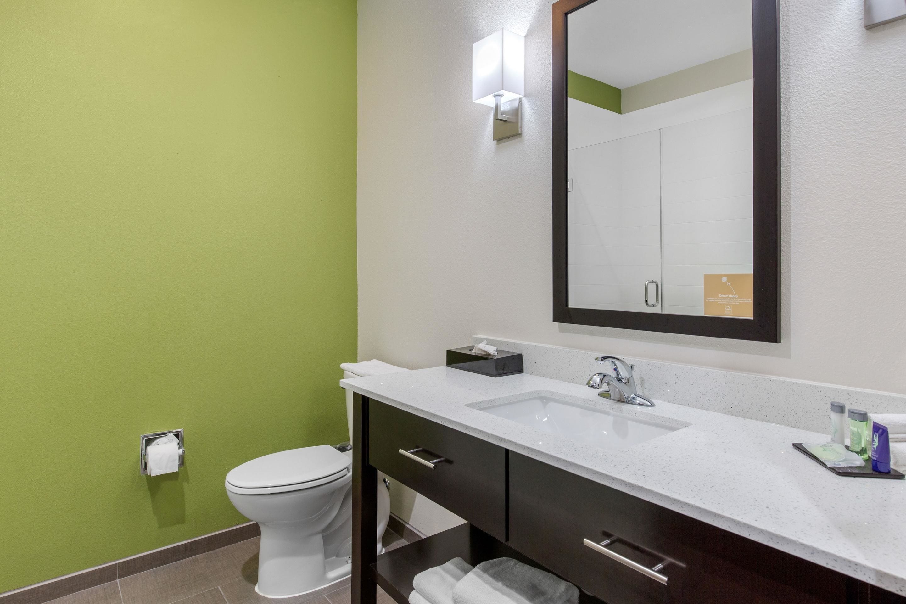 Un baño con inodoro blanco, lavamanos, espejo y toallero.