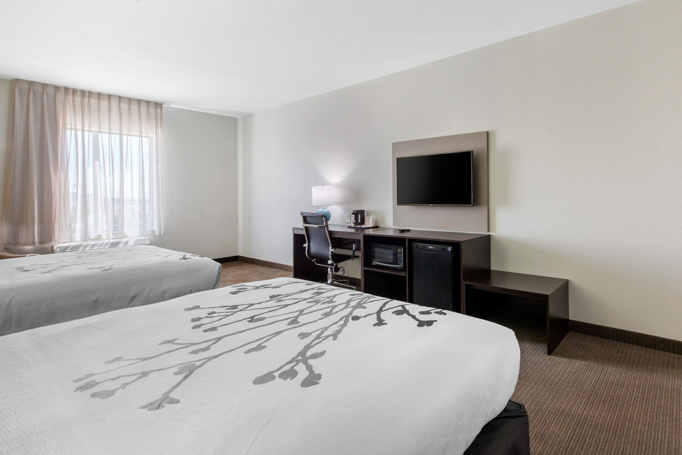A hotel room with two beds, a desk, a chair, a television, and a window with curtains.