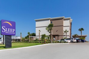 A Sleep Inn & Suites sign, a parking lot, and a building with palm trees.
