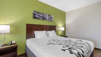 A hotel room with a large bed, green walls, a wooden headboard, white bedding, a bedside table with a lamp, and a phone.