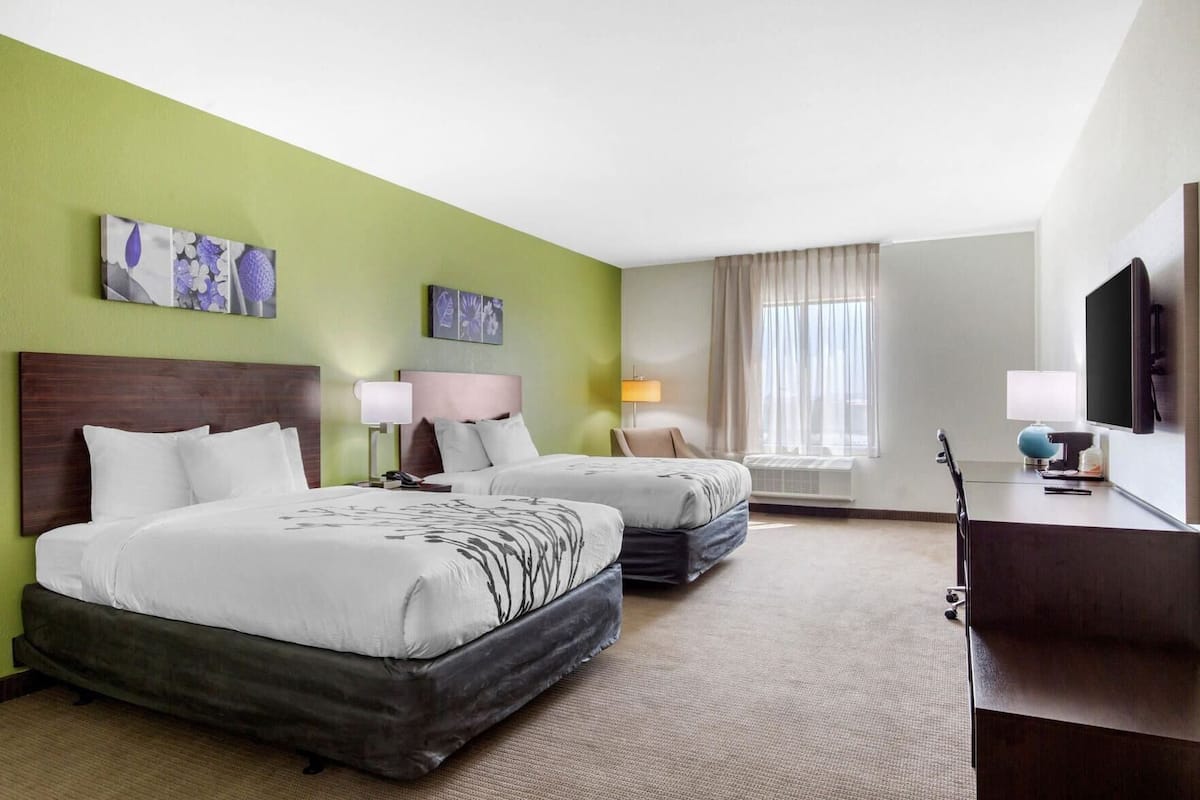 Ein Hotelzimmer mit zwei Betten, einem Schreibtisch, einem Fernseher und Kunstwerken an den Wänden.