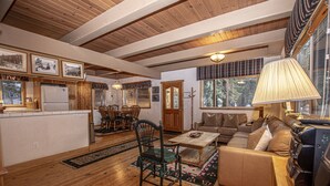 A cozy living room with a wooden floor, a sofa, a coffee table, and a dining area with chairs and a table. - Willow by Hauserman Rentals (Tahoe City)