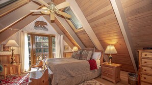 A cozy attic bedroom with a sloped ceiling, a bed with a quilted blanket, a wooden dresser, a nightstand with a lamp, and a window with curtains. - Willow by Hauserman Rentals (Tahoe City)