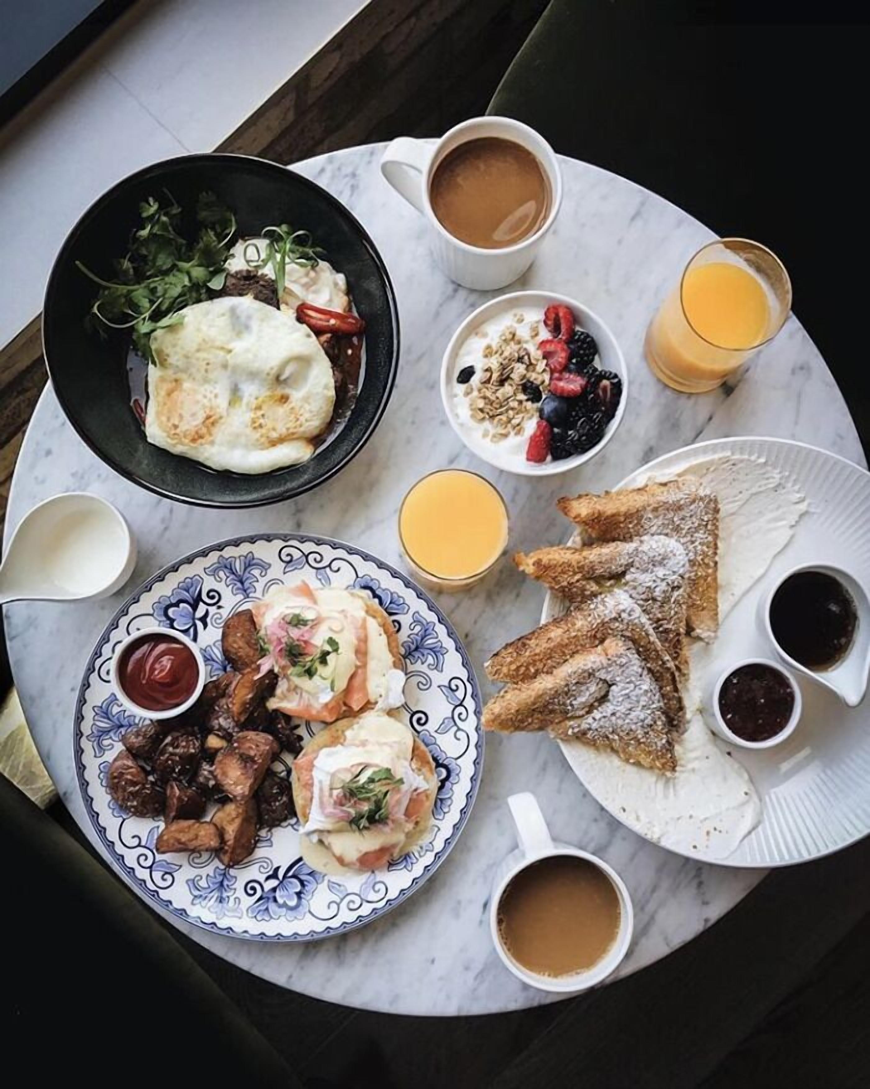 Una mesa de mármol con un desayuno que incluye huevos, tostadas, fruta y café.
