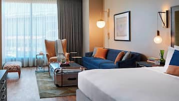 Habitación de hotel con una cama grande, un sofá azul, una silla, una mesita y una maleta.