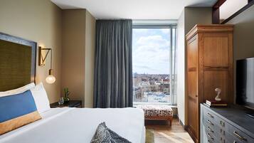 Habitación de hotel con una cama grande, un armario de madera, un televisor y vista a la ciudad a través de una ventana.