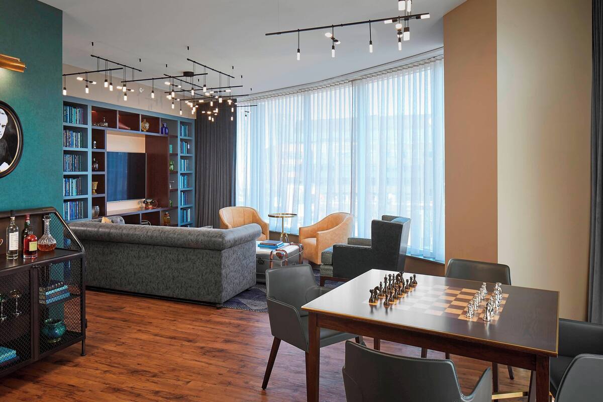 Una sala de estar moderna con una mesa de ajedrez, una estantería y un rincón de estar con sofá y sillones.