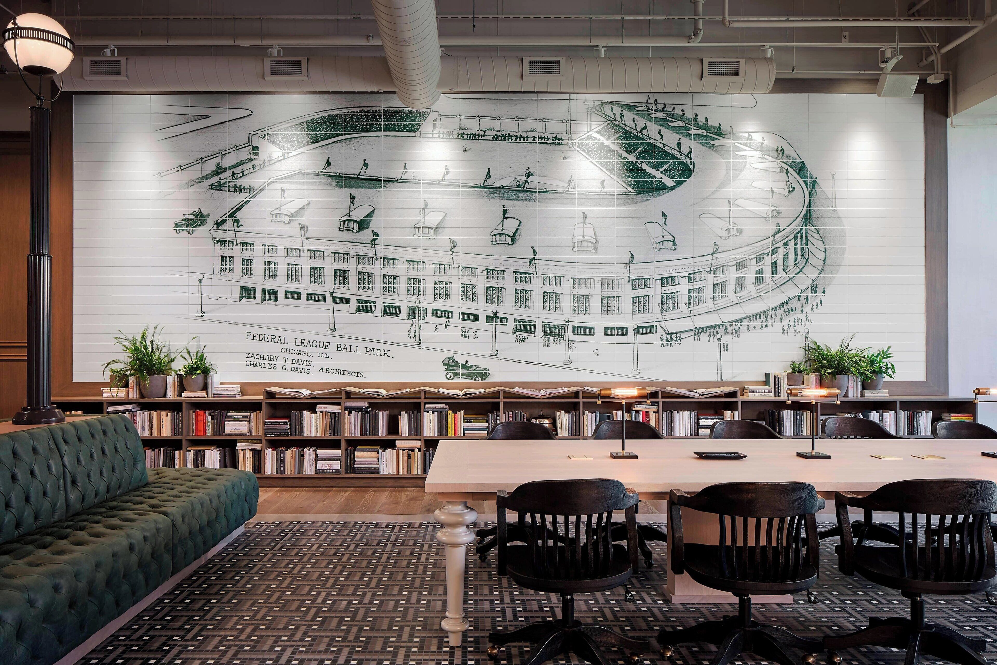 A library with a large mural, bookshelves, a sofa, and a table with chairs.