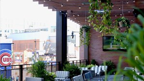 An outdoor seating area with tables and chairs, potted plants, and a TV screen. - Hotel Zachary Chicago, a Tribute Portfolio Hotel (Chicago)
