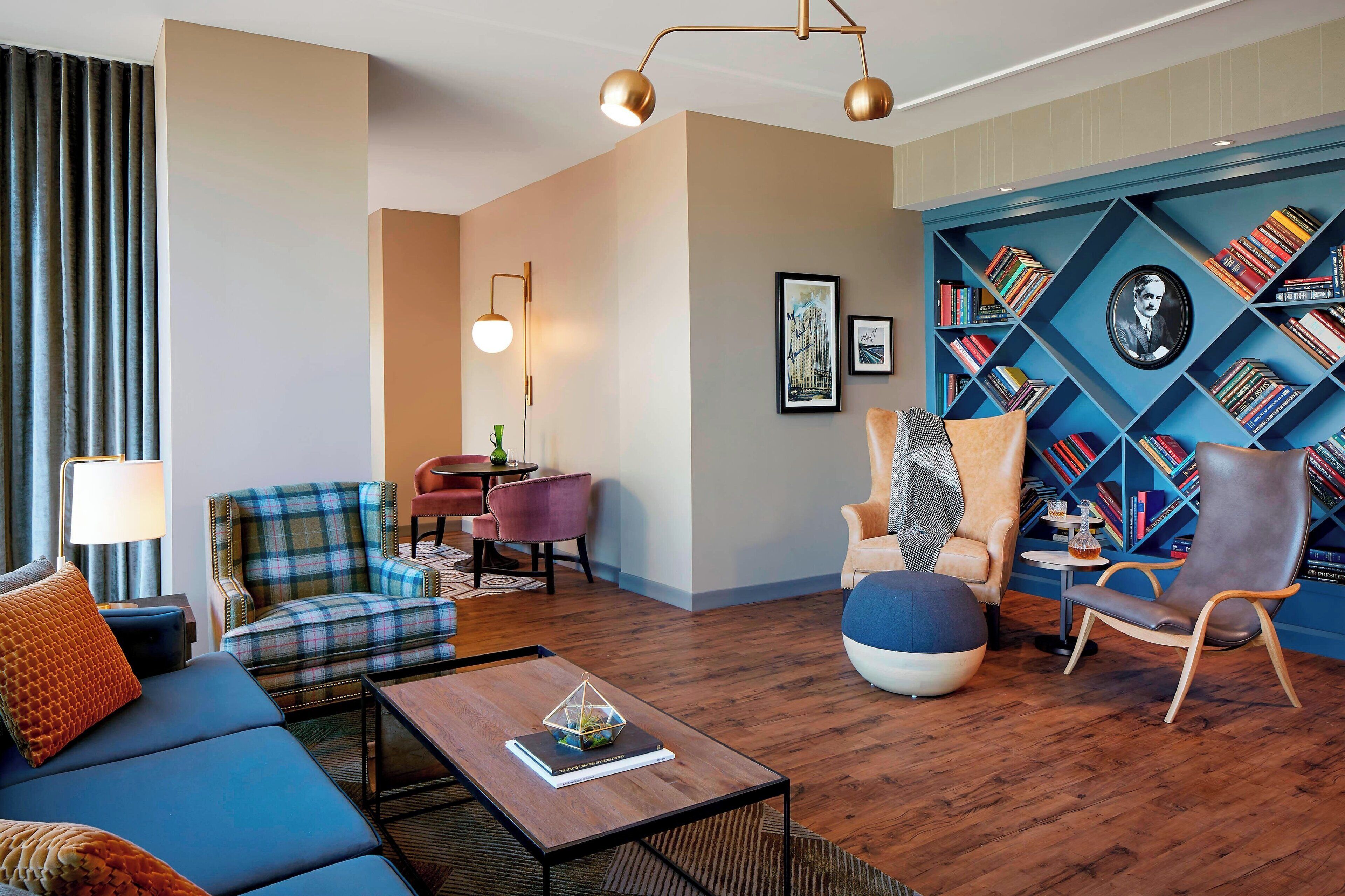 Una sala de estar moderna con un sofá azul, un sillón escocés, una mesa de centro de madera y una estantería llena de libros.