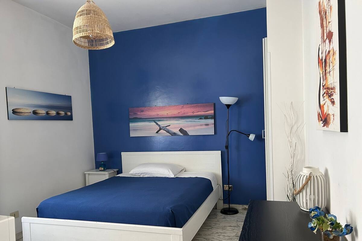 A bedroom with a bed, a nightstand, a lamp, and artwork on the walls.
