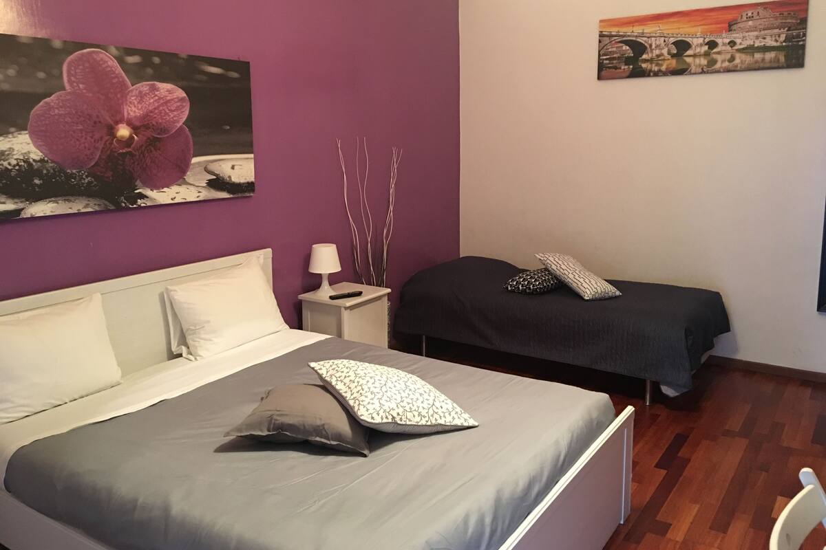 A bedroom with a bed, two bedside tables, a nightstand, a lamp, and a painting on the wall.